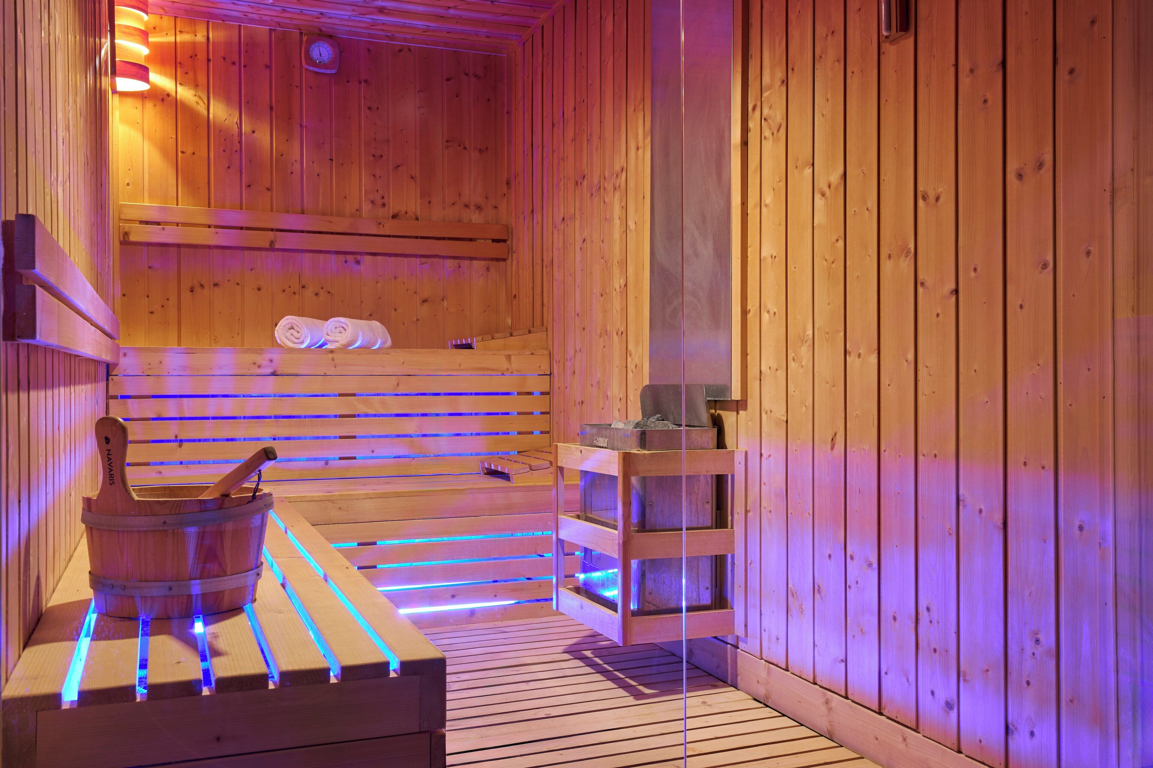 A wooden sauna with benches, a wooden bucket, and shelves with towels.