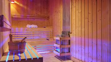 A wooden sauna with benches, a wooden bucket, and shelves with towels.