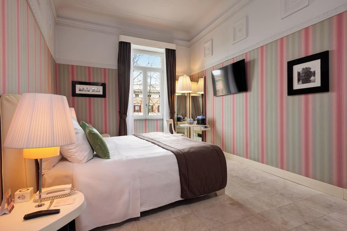 A hotel room with a bed, bedside table, lamp, and a window with curtains.