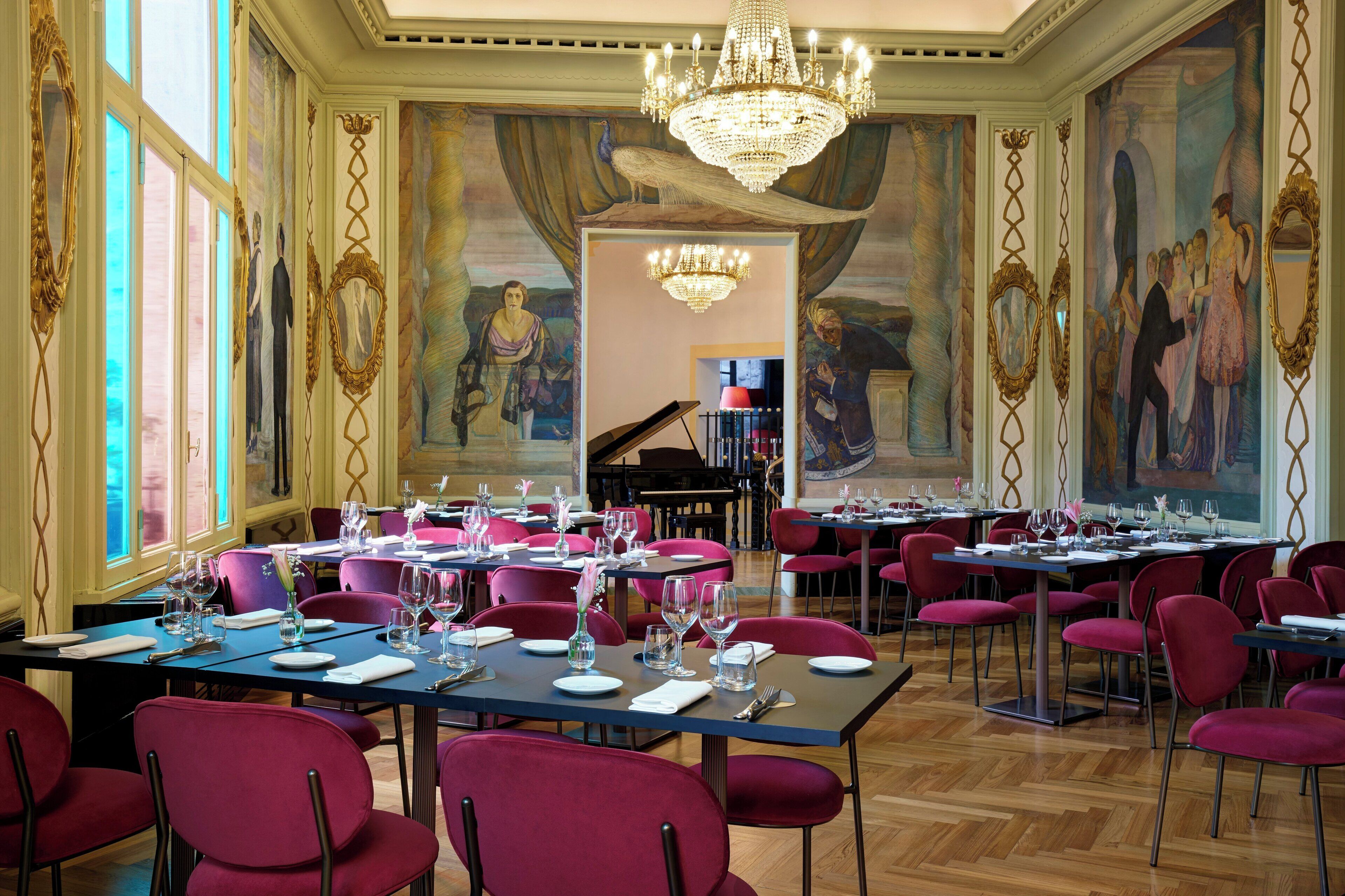 A formal dining room with tables set for service, large windows, and a grand chandelier.