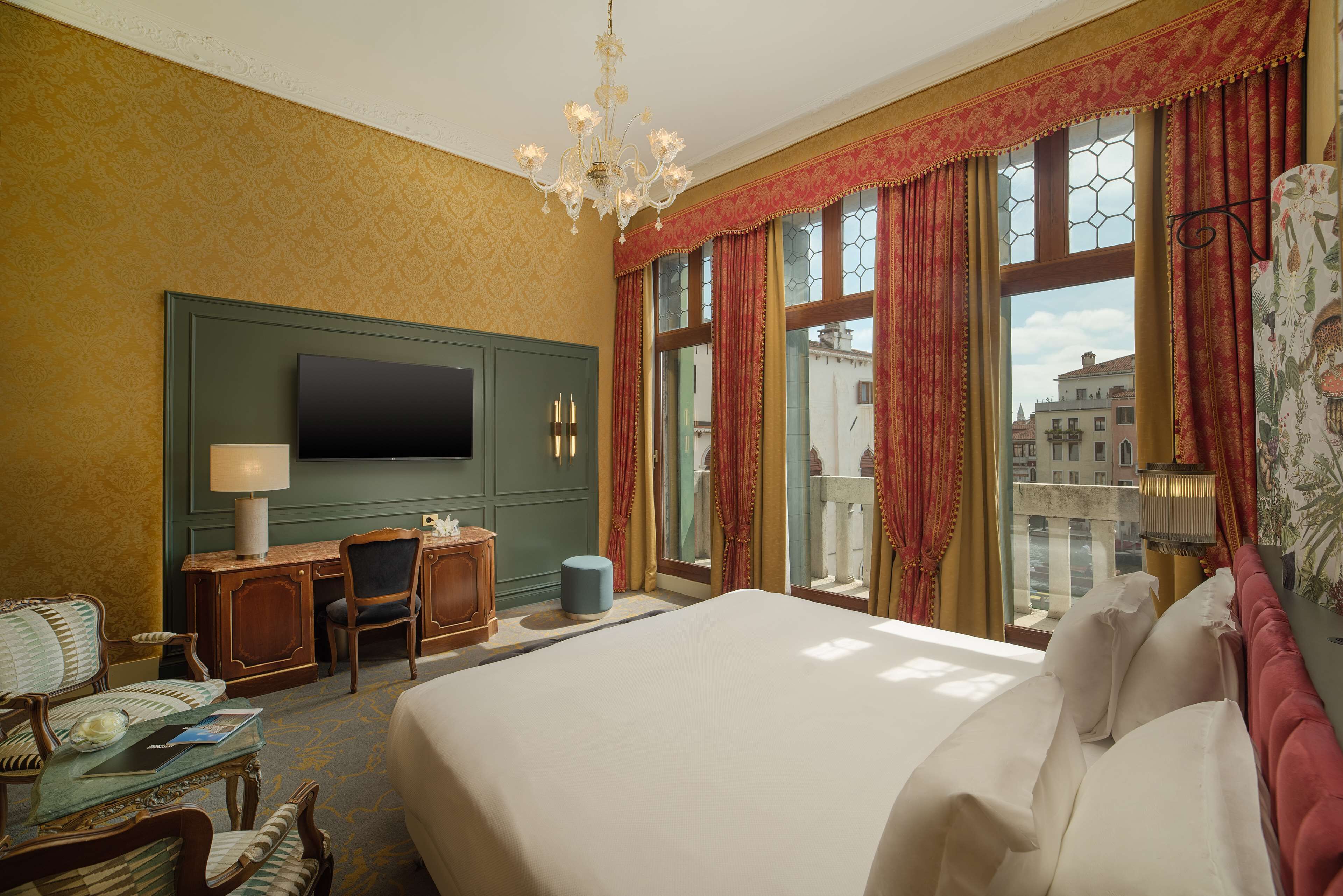 A hotel room with a large bed, a desk with a chair, a television, and a window with curtains.
