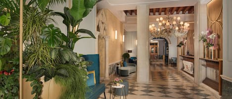 Un vestíbulo de hotel con suelo a cuadros, un sofá azul, una mesa redonda y una gran planta en maceta.