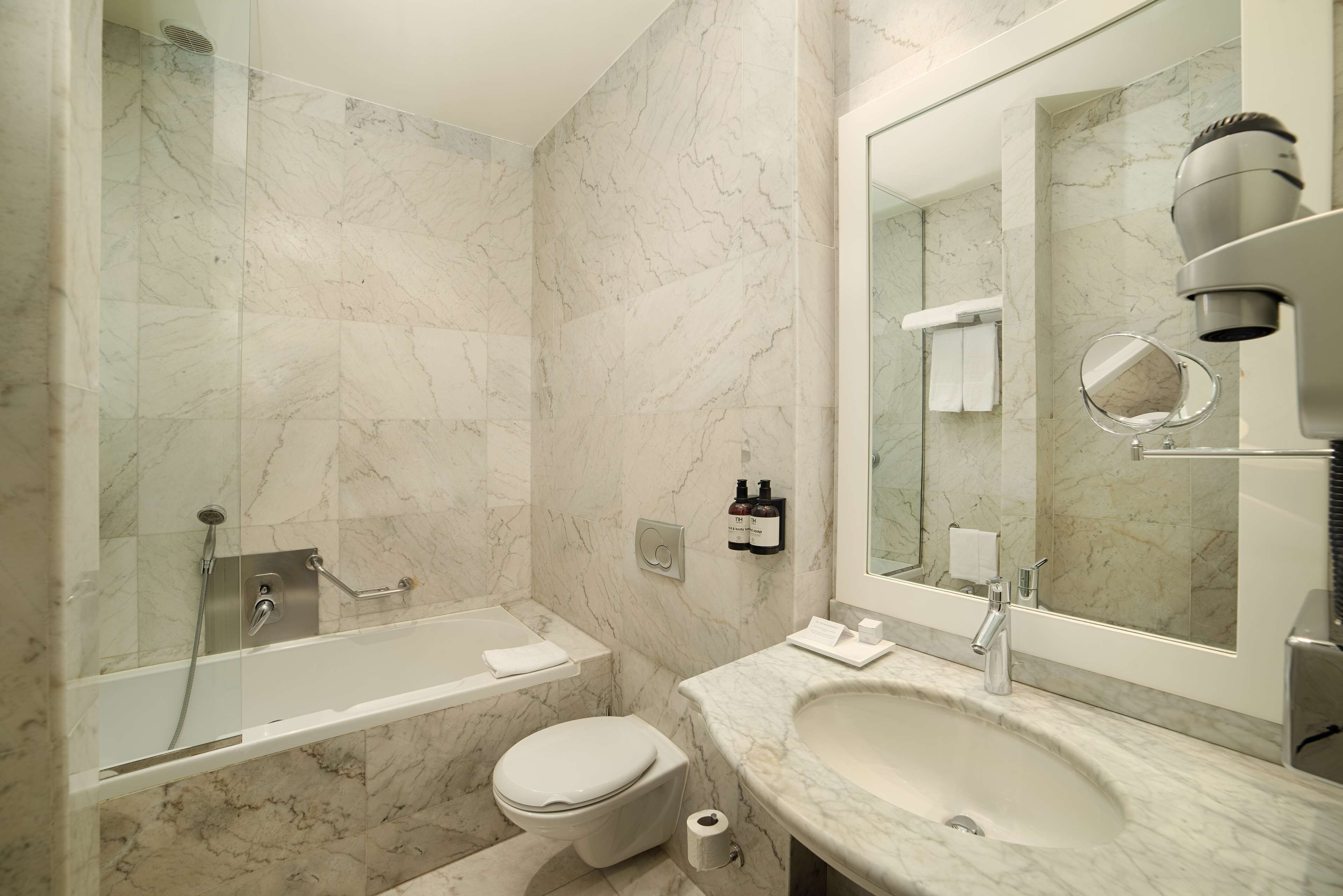 Ein modernes Badezimmer mit einer gläsernen Duschkabine, einer Badewanne, einer Toilette und einem Waschbecken mit großem Spiegel.
