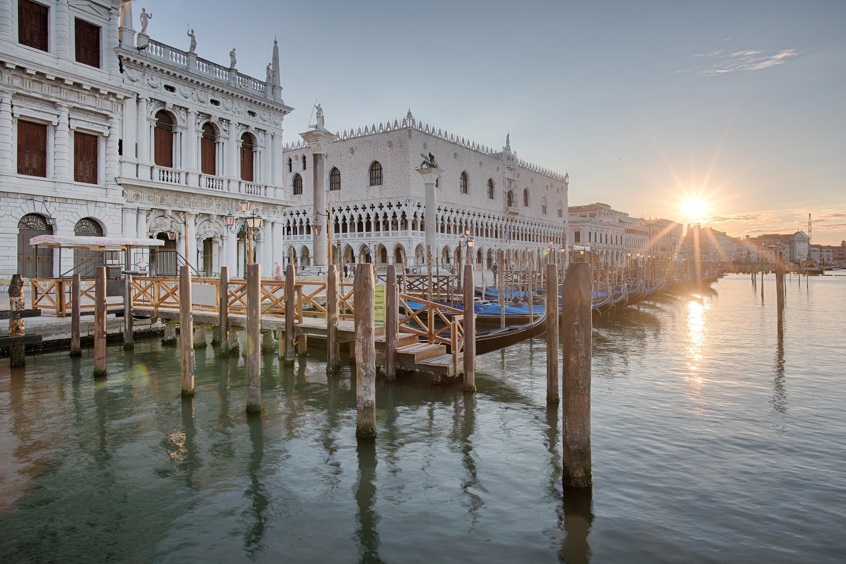 A historic building with a waterfront view, featuring a wooden walkway over water, and a sunset in the background.