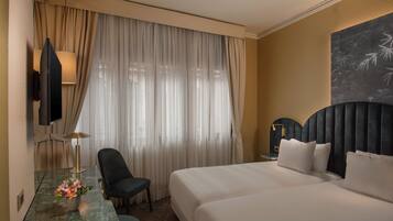 Habitación de hotel con una cama grande, un escritorio con lámpara, una silla y un televisor.