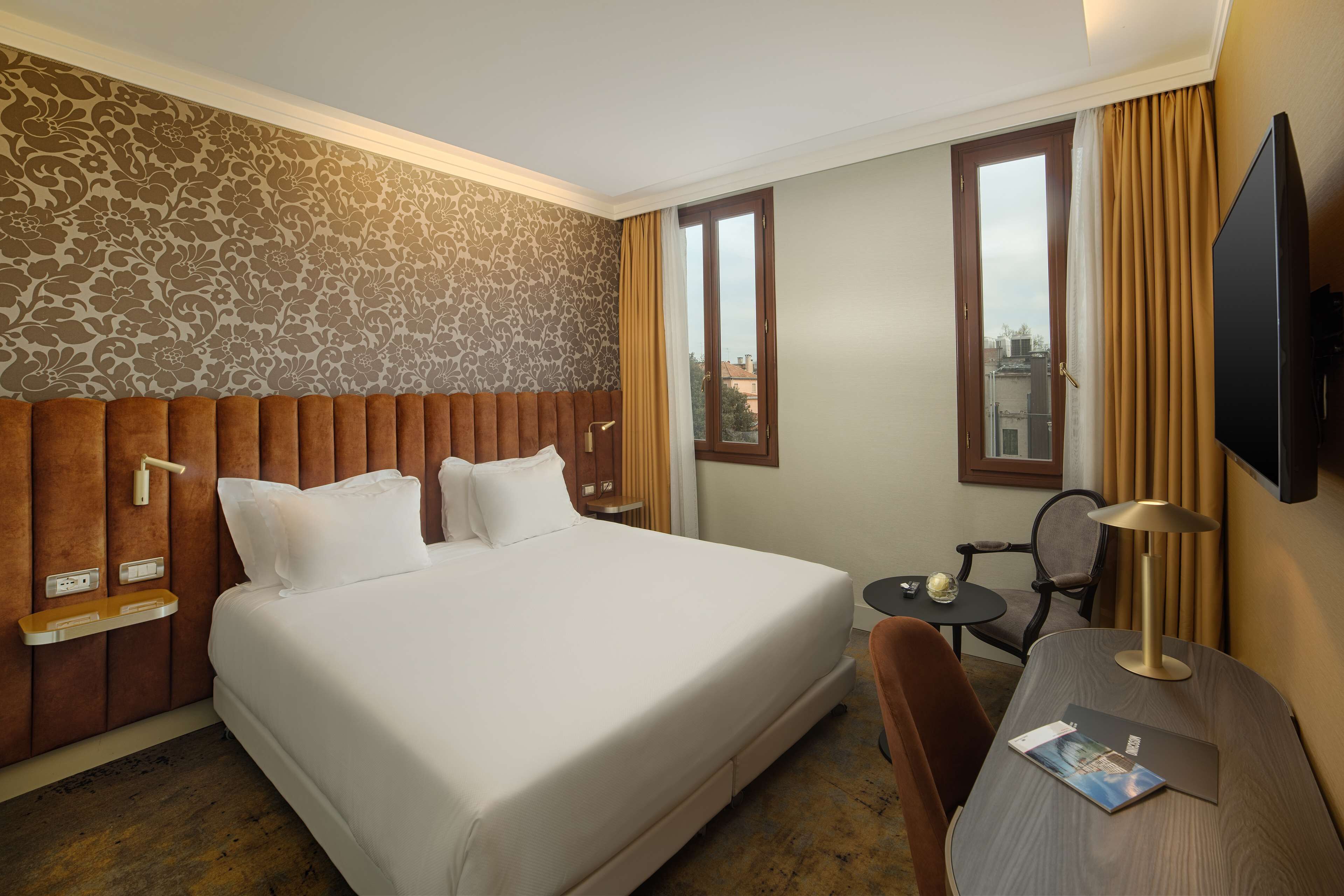 A hotel room with a large bed, a desk with a lamp, a chair, and a television.