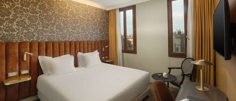 A hotel room with a large bed, a desk with a lamp, a chair, and a television.