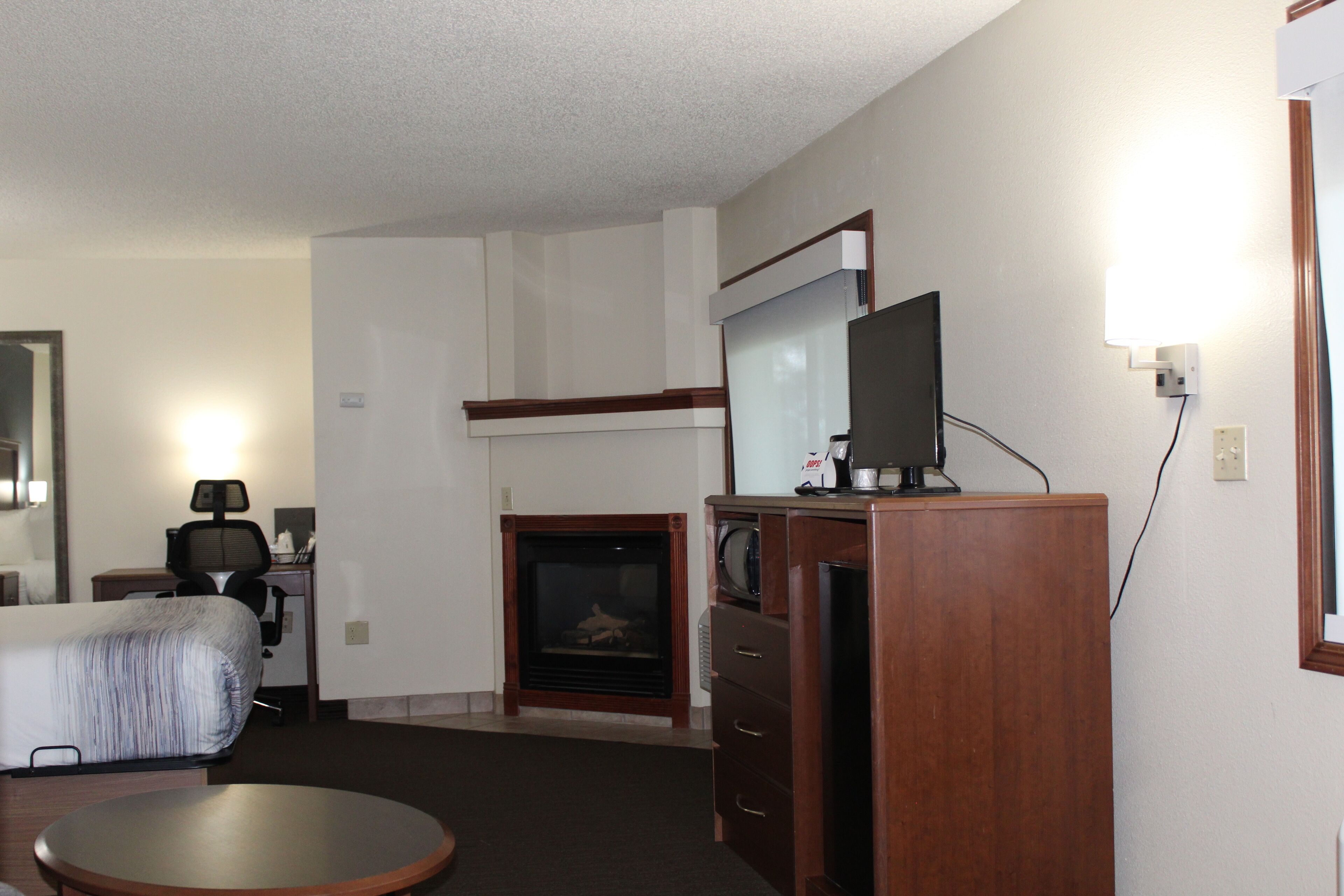 A hotel room with a bed, a desk with a chair, a television on a wooden cabinet, and a fireplace.
