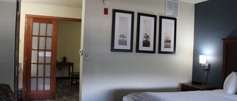 A hotel room with a bed, a chair, a desk, and a door.