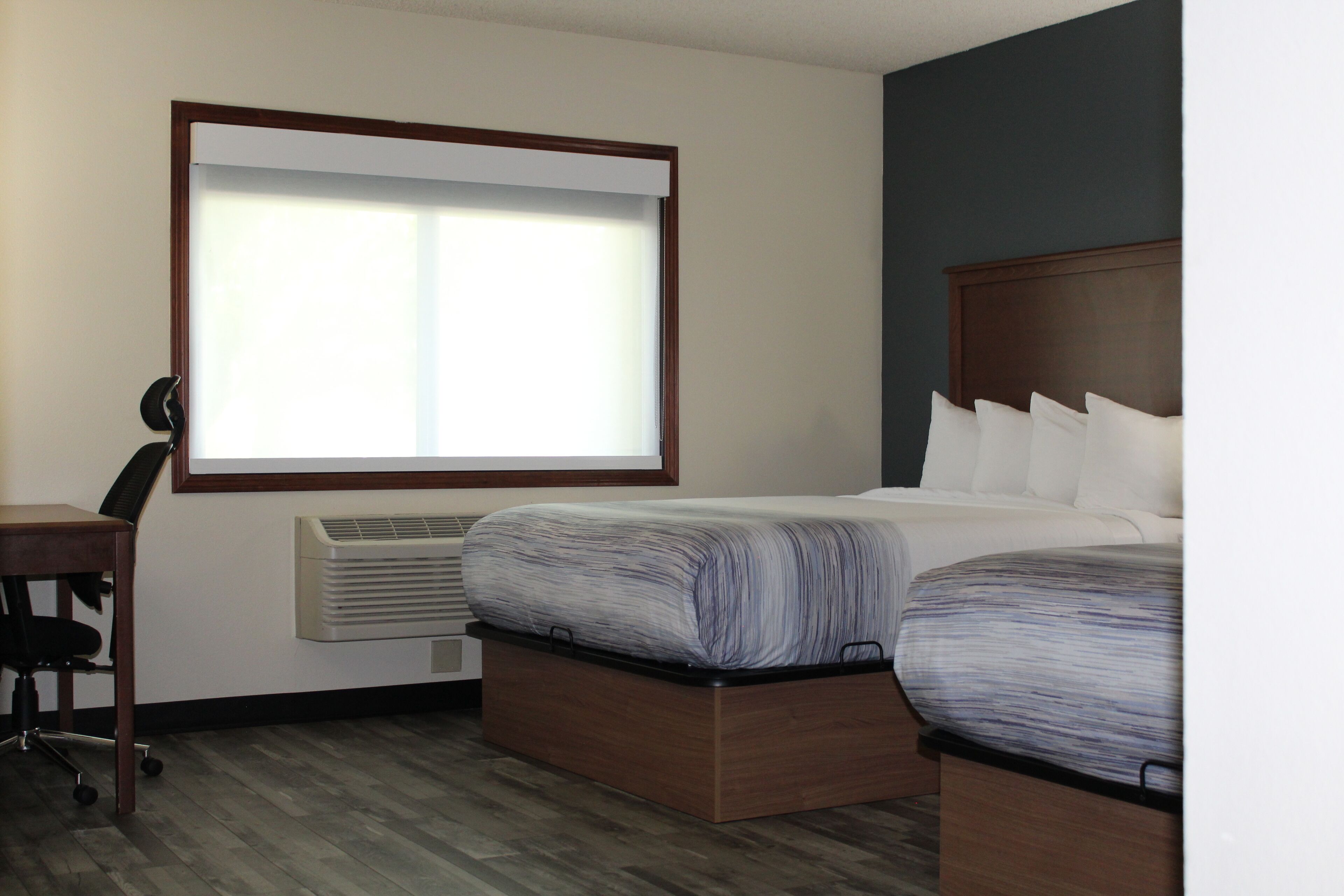 A hotel room with a bed, a desk, and a window with blinds.