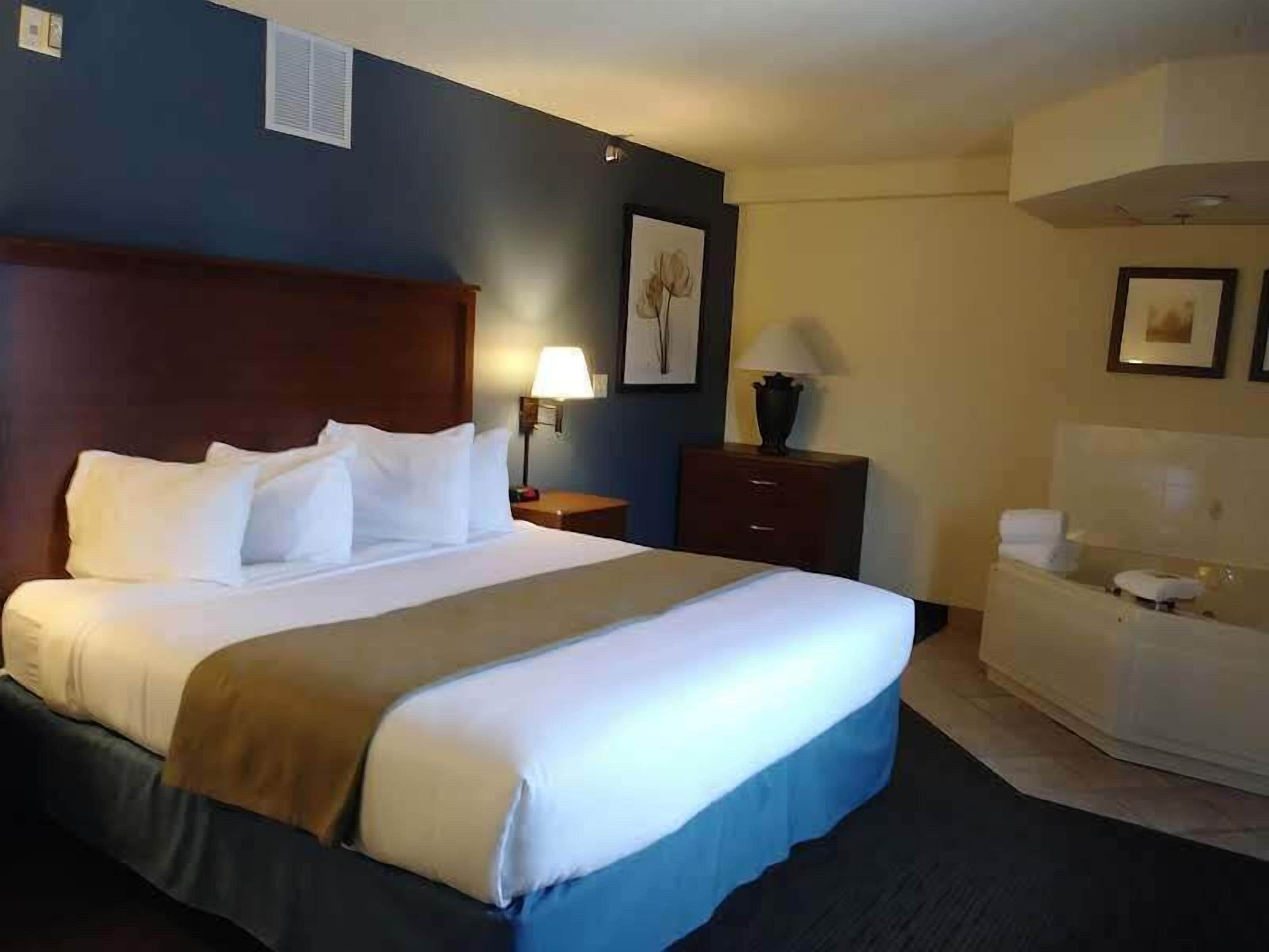 Ein Hotelzimmer mit einem großen Bett, einem Nachttisch, einer Kommode und einem Badezimmer mit Toilette und Waschbecken.