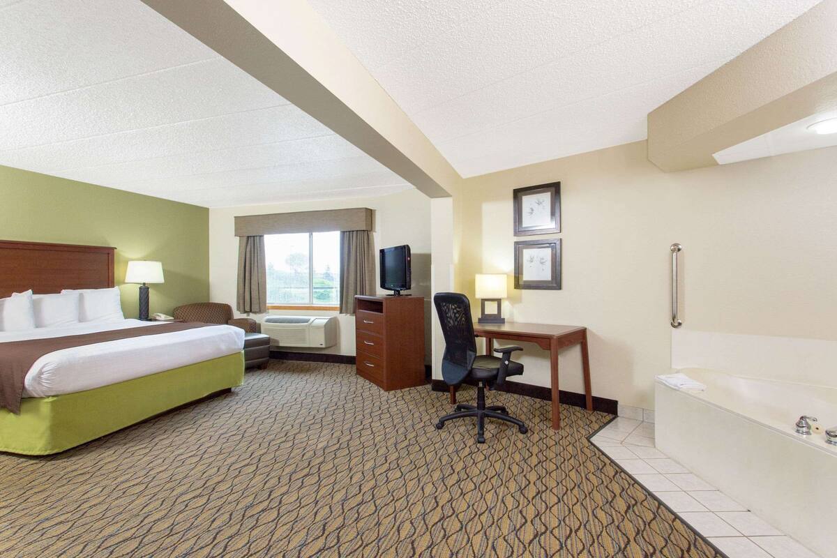 Habitación de hotel con cama, escritorio, silla, televisor y baño con bañera.