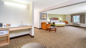 A hotel room with a bed, a desk with a sink, a chair, a small table, and a window with curtains. - AmericInn by Wyndham Sheboygan (Sheboygan)