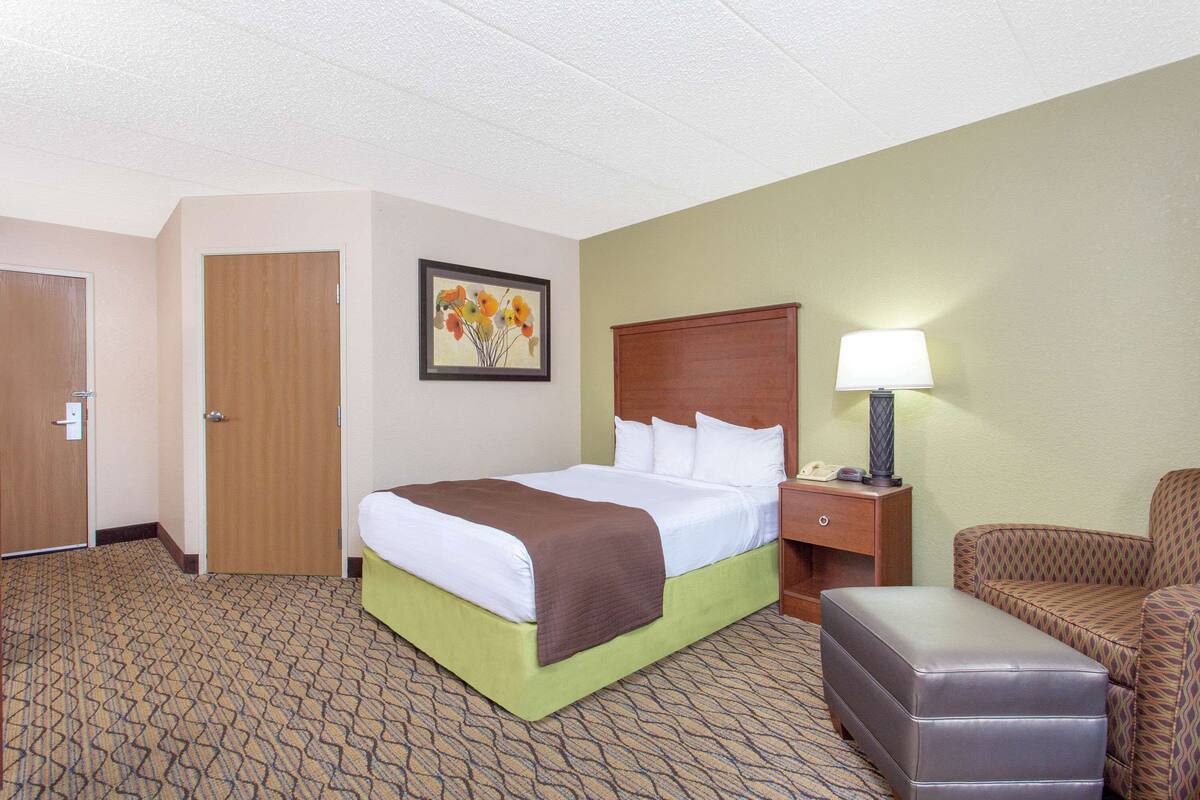 Una habitación de hotel con una cama, una mesita de noche, una lámpara, una silla y una puerta.