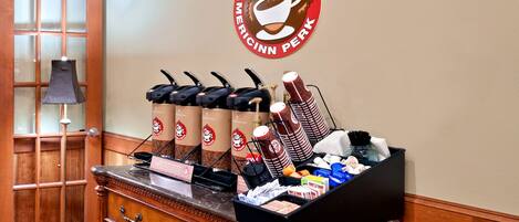 A coffee station with multiple coffee dispensers and a sign for Americinn Perk.