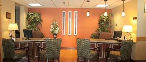 A reception area with a reception desk, two computer monitors, a telephone, and four patterned chairs.