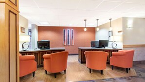 A reception area with two desks, a TV, and orange chairs. - AmericInn by Wyndham Sheboygan (Sheboygan)