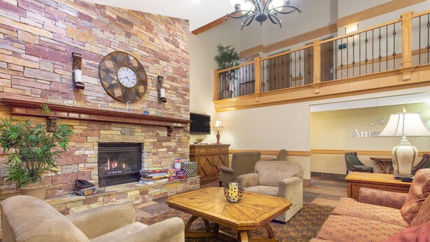 A spacious living area with a stone fireplace, comfortable seating, and a balcony with a railing. - AmericInn by Wyndham Sheboygan (Sheboygan)