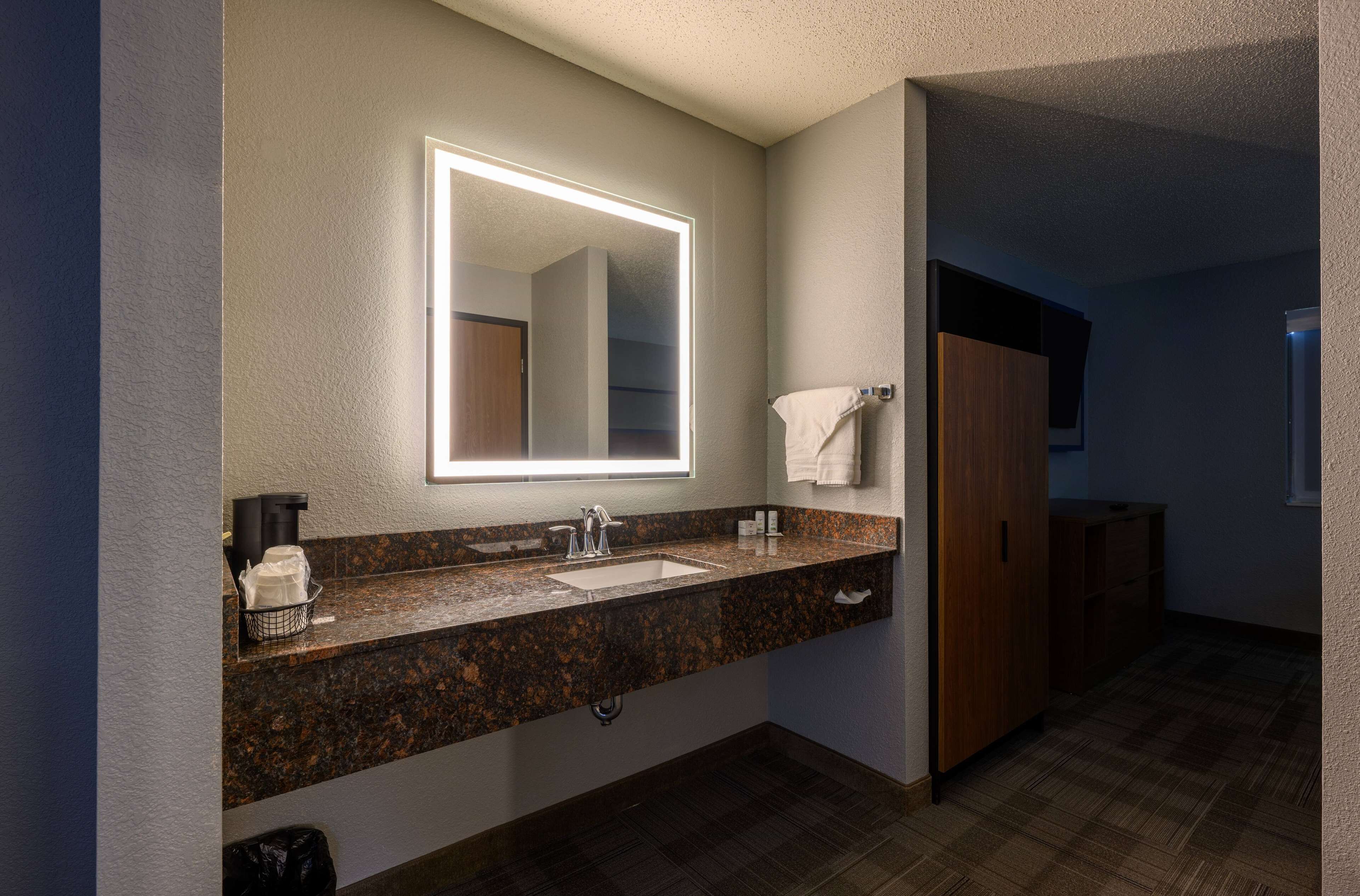 A bathroom with a granite countertop, a sink, a mirror with a light, and a towel rack.