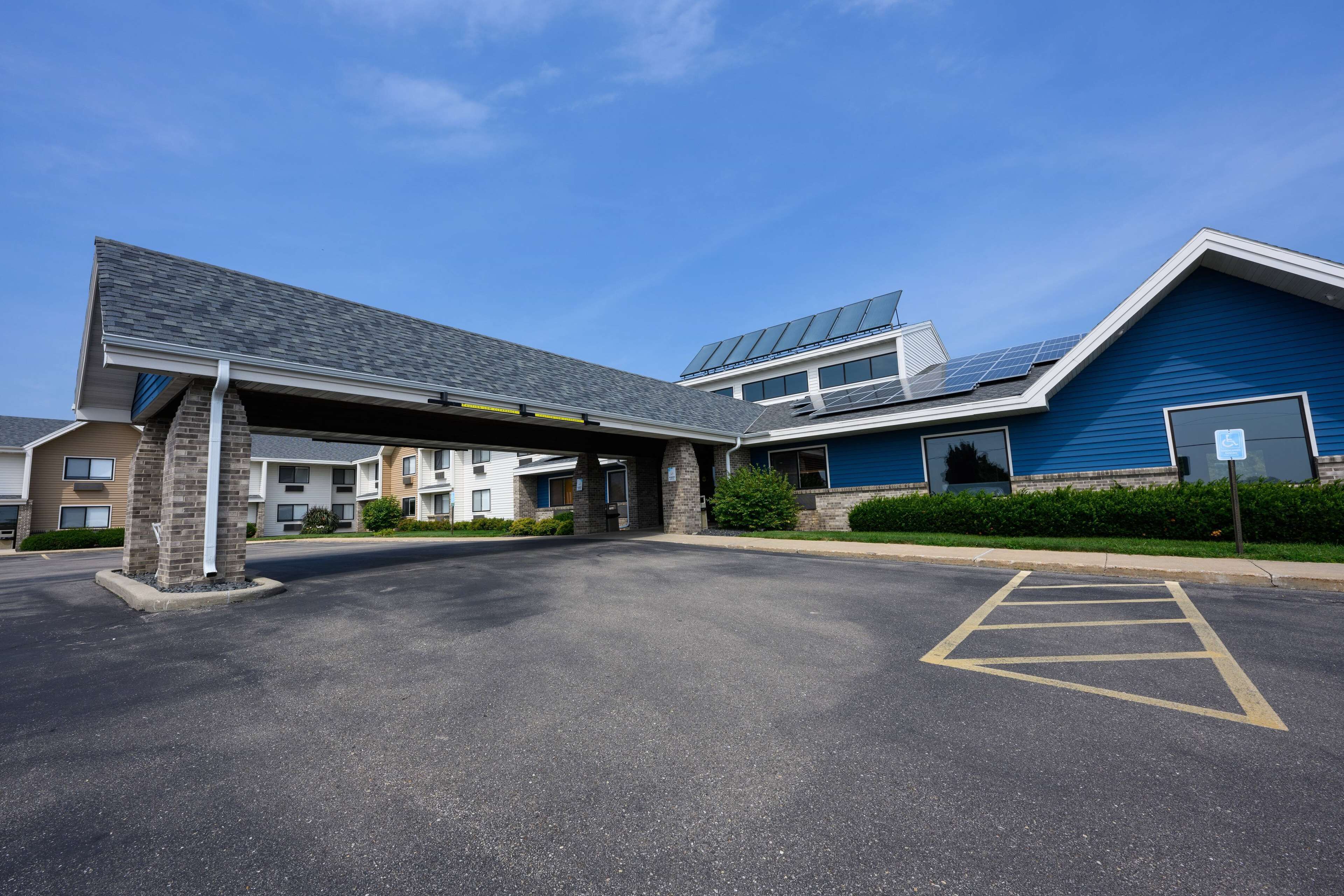 A parking lot with a building entrance, a covered walkway, and a blue building with solar panels.
