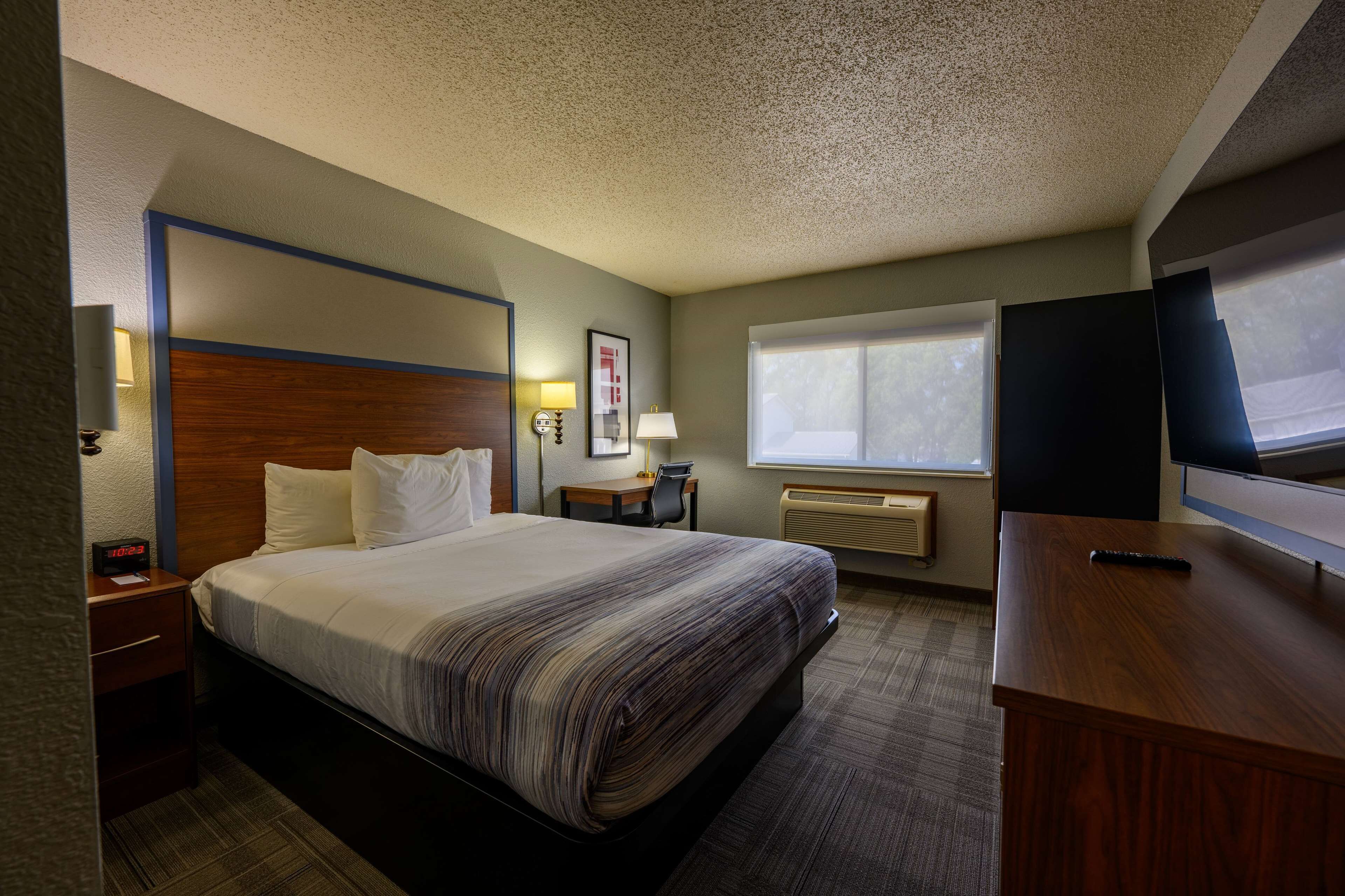 A hotel room with a bed, bedside table, lamp, desk, and a TV.
