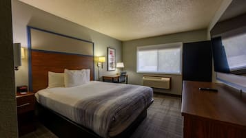 A hotel room with a bed, bedside table, lamp, desk, and a TV.