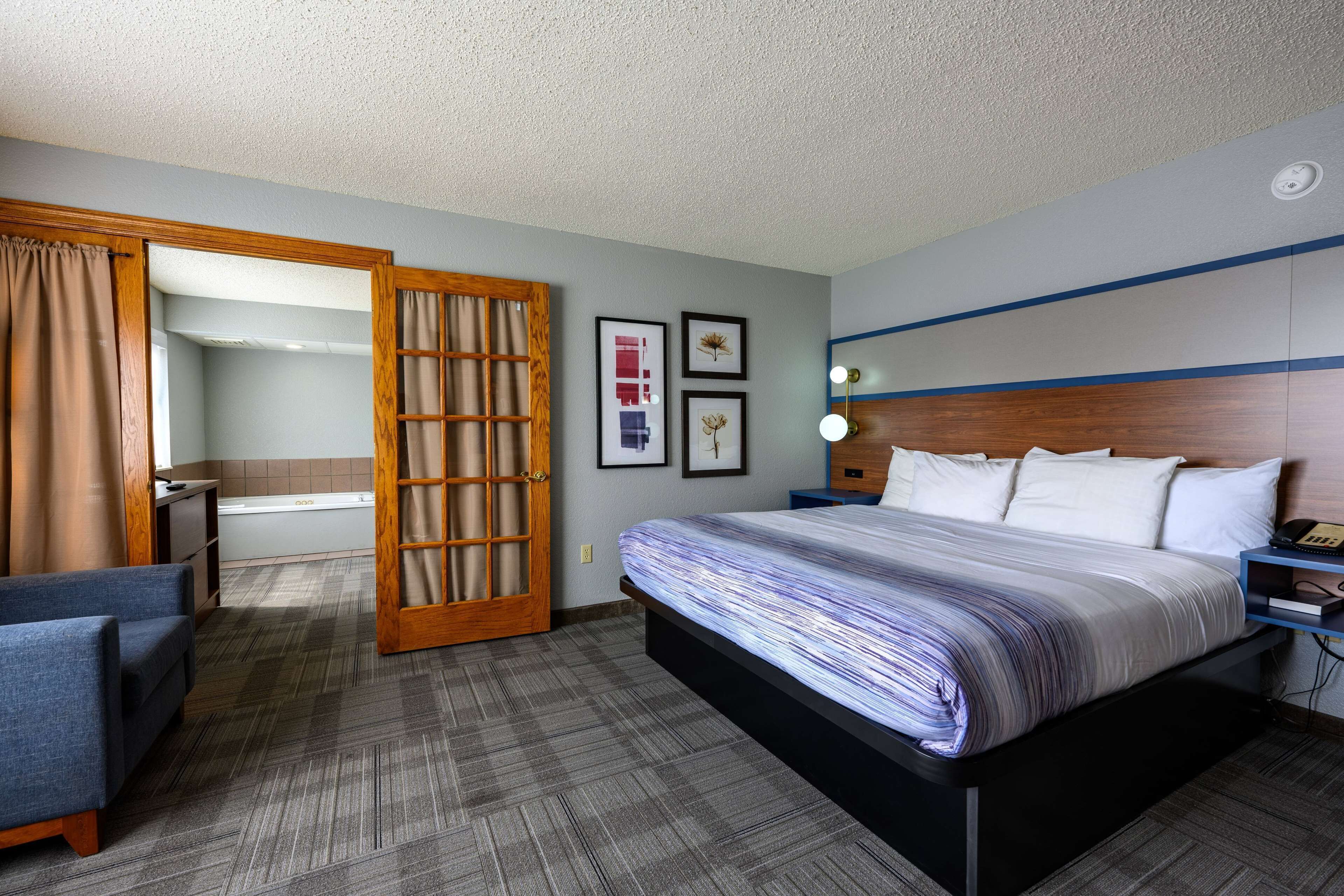 Quarto de hotel com cama, escrivaninha, cadeira, banheiro e porta.