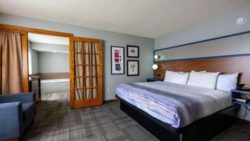 Quarto de hotel com cama, escrivaninha, cadeira, banheiro e porta.