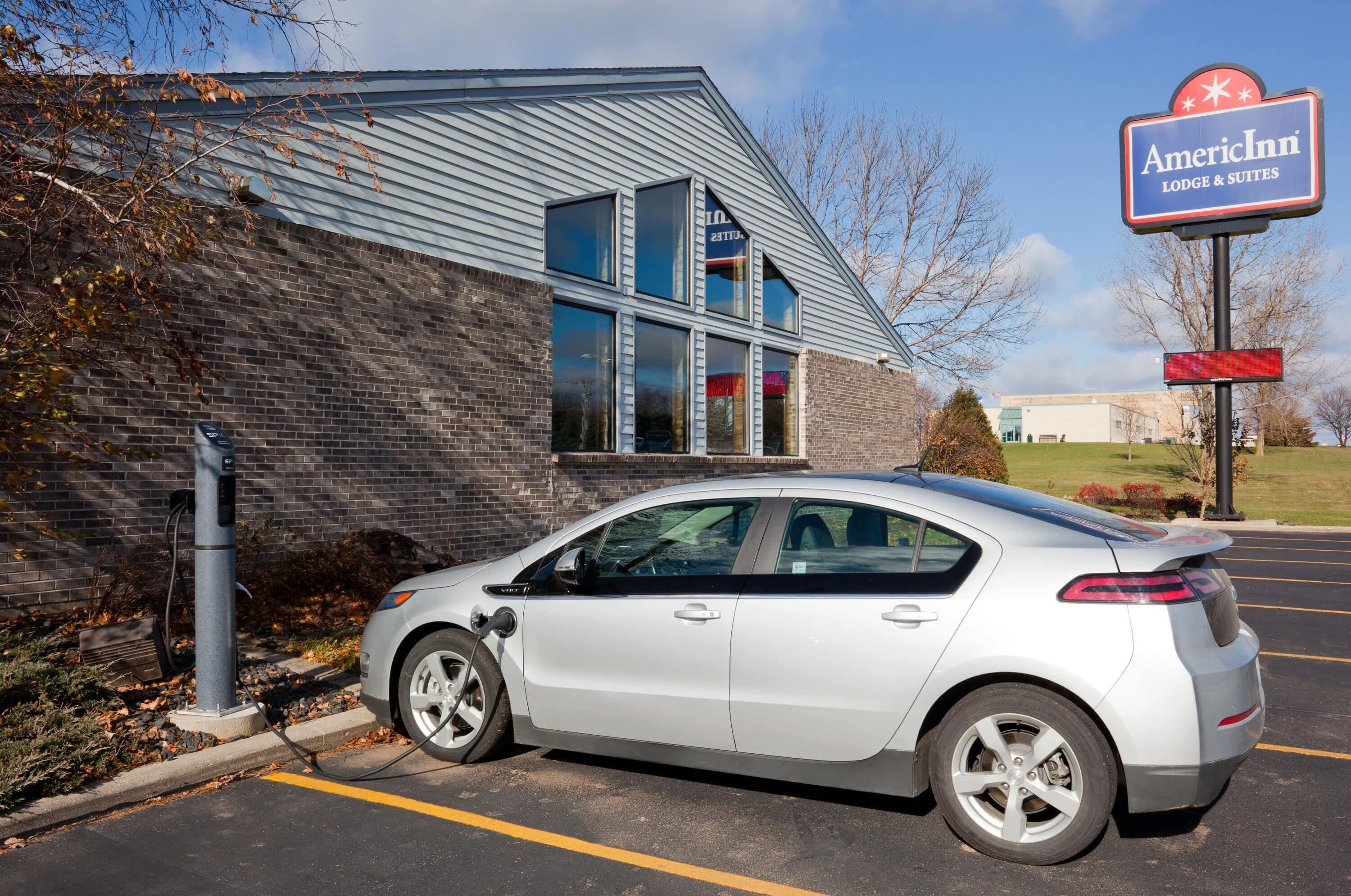 A silver car parked in a parking lot with a brick building and a sign for American Inn Lodge & Suites in the background.