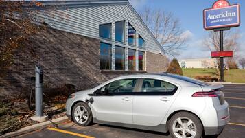 A silver car parked in a parking lot with a brick building and a sign for American Inn Lodge & Suites in the background.