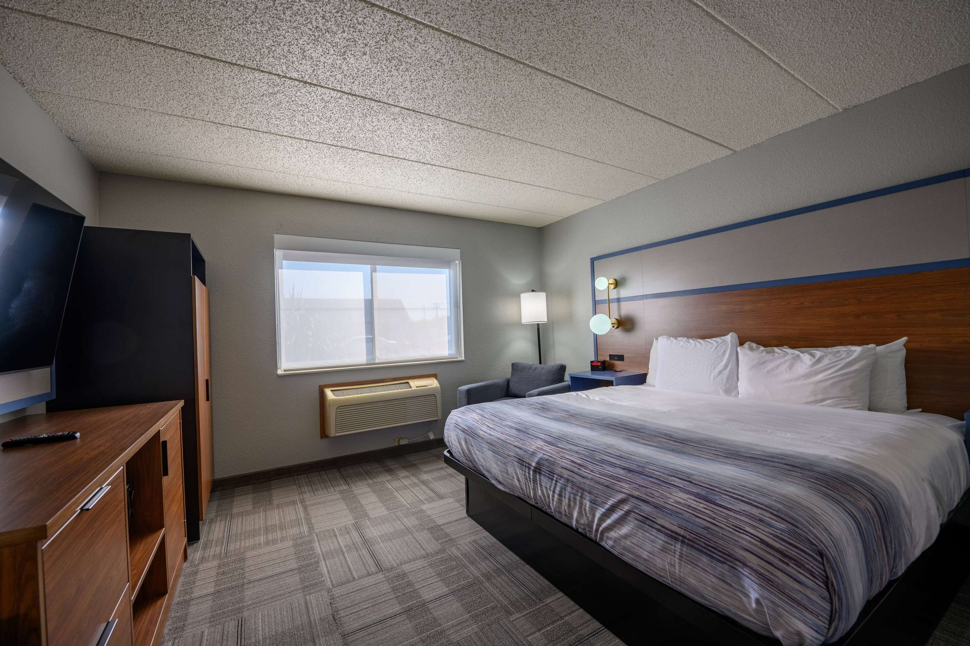 A hotel room with a large bed, a desk with a TV, a window, and a nightstand with a lamp.