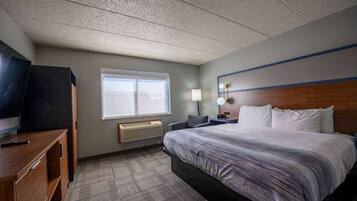 A hotel room with a large bed, a desk with a TV, a window, and a nightstand with a lamp.
