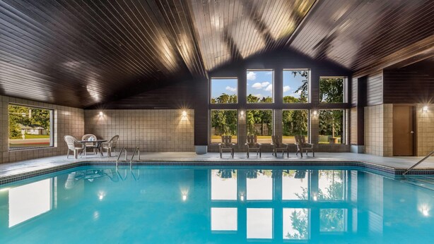 An indoor swimming pool with wooden ceiling, large windows, and a tiled wall. - Baymont by Wyndham Bloomington MSP Airport (Richfield)