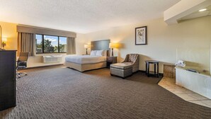 A hotel room with a bed, desk, chair, and a small table. - Baymont by Wyndham Bloomington MSP Airport (Richfield)