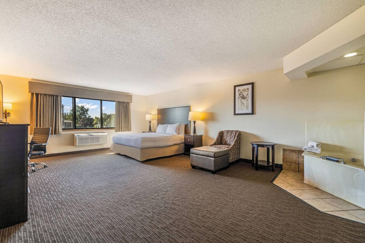 A hotel room with a bed, desk, chair, and a small table.