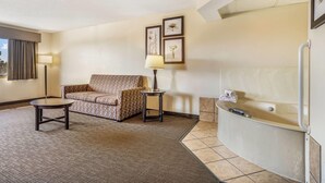 A hotel room with a sofa, a small table, a lamp, and a bathtub. - Baymont by Wyndham Bloomington MSP Airport (Richfield)