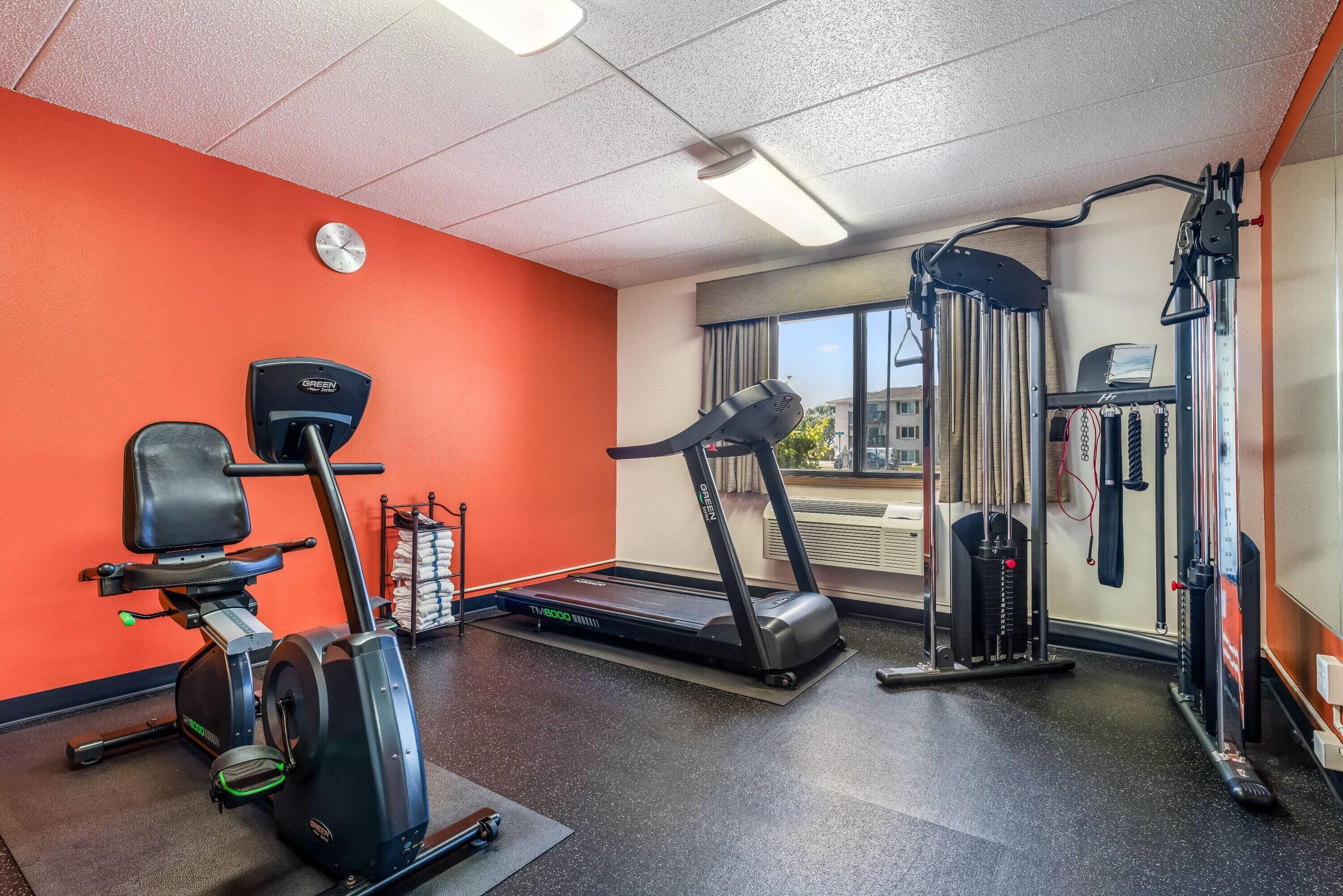 A gym with a treadmill, elliptical, and weight machine.