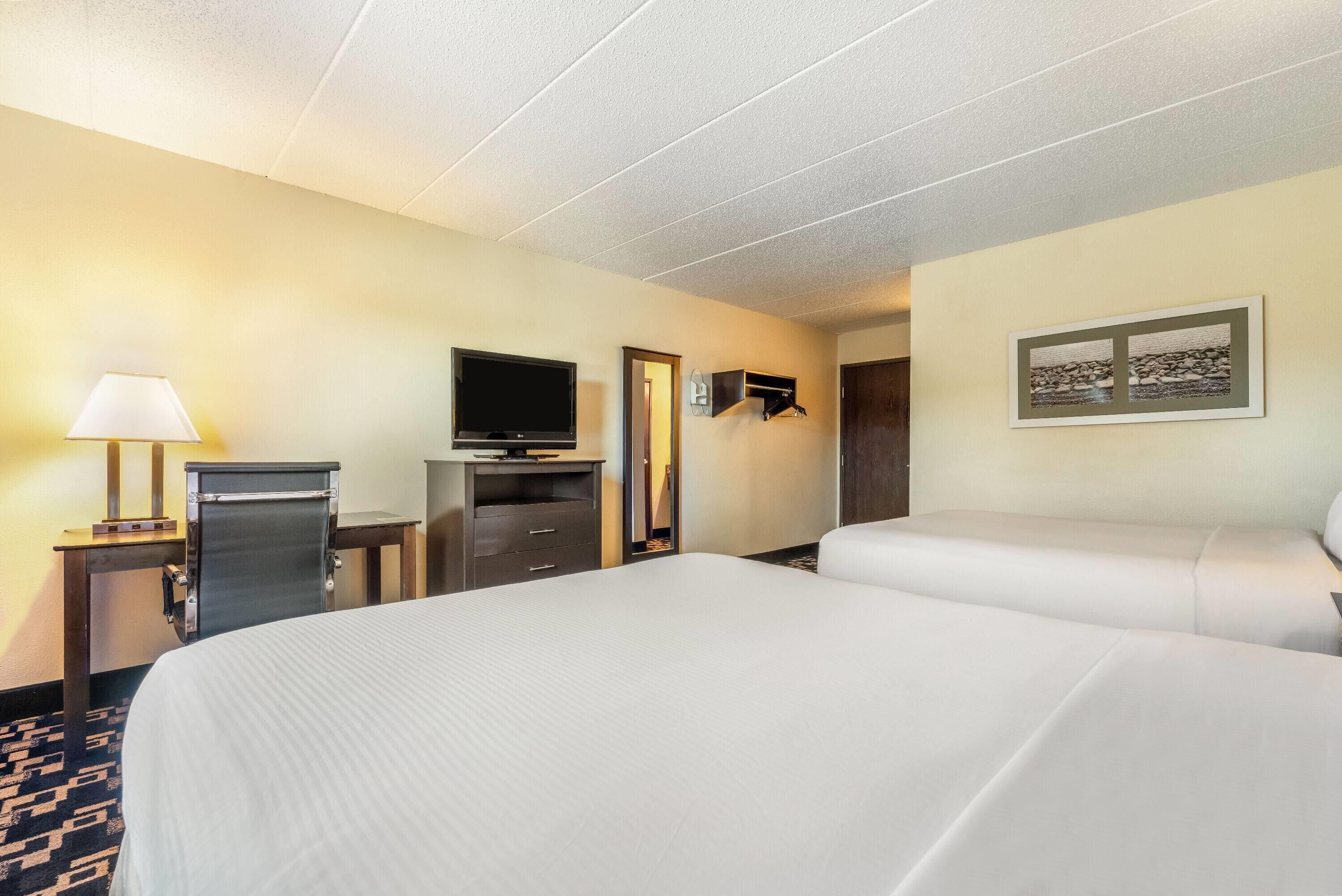 Habitación de hotel con una cama grande, un escritorio con lámpara, televisión y un cuadro en la pared.