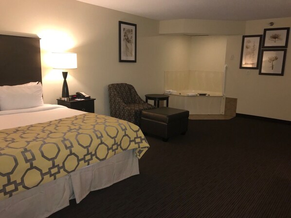 A hotel room with a bed, a chair, a small table, a lamp, and a bathtub.