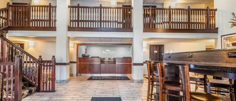 A hotel lobby with a reception desk, a staircase, and a dining area with wooden furniture.