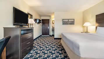 A hotel room with a large bed, a TV on a dresser, a desk with a chair, and a patterned carpet.