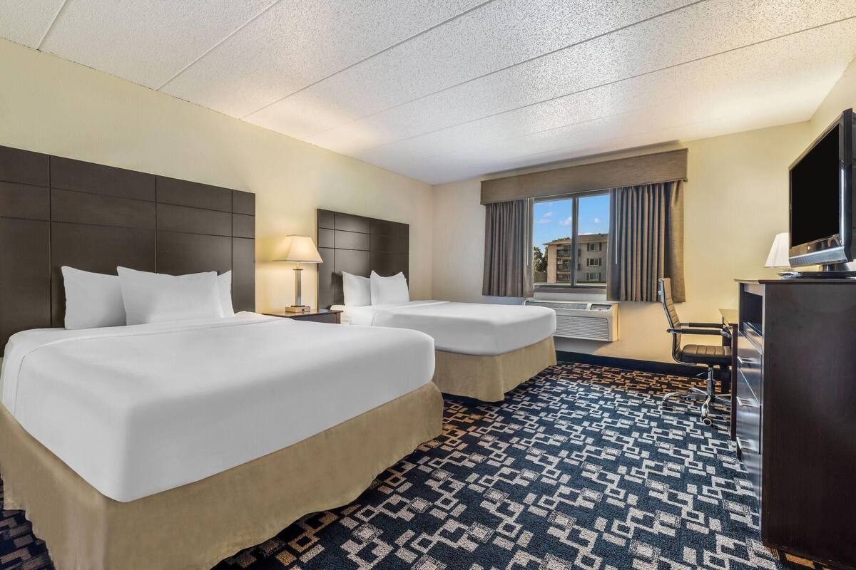 A hotel room with two beds, a TV, a desk, and a window with curtains.