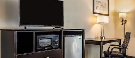 Habitación de hotel con televisión de pantalla plana, microondas, refrigerador pequeño, escritorio con lámpara y una silla.