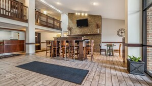 A spacious lobby with a central bar area, a staircase, and a brick wall with a television. - Baymont by Wyndham Bloomington MSP Airport (Richfield)