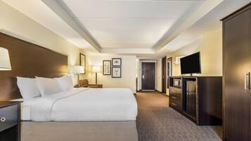 Una habitación de hotel con una cama grande, televisión, cómoda y una puerta que da a un pasillo.