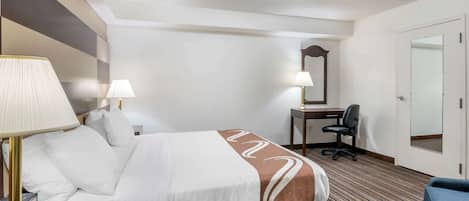 Une chambre d’hôtel avec un lit, des lampes de chevet, un bureau avec une chaise, un miroir et une porte.