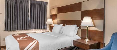 Habitación de hotel con una cama grande, dos lámparas de noche, un cabecero de madera y un sillón azul.