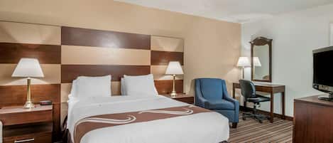 A hotel room with a large bed, two bedside tables with lamps, a desk with a chair, a television, and a mirror.