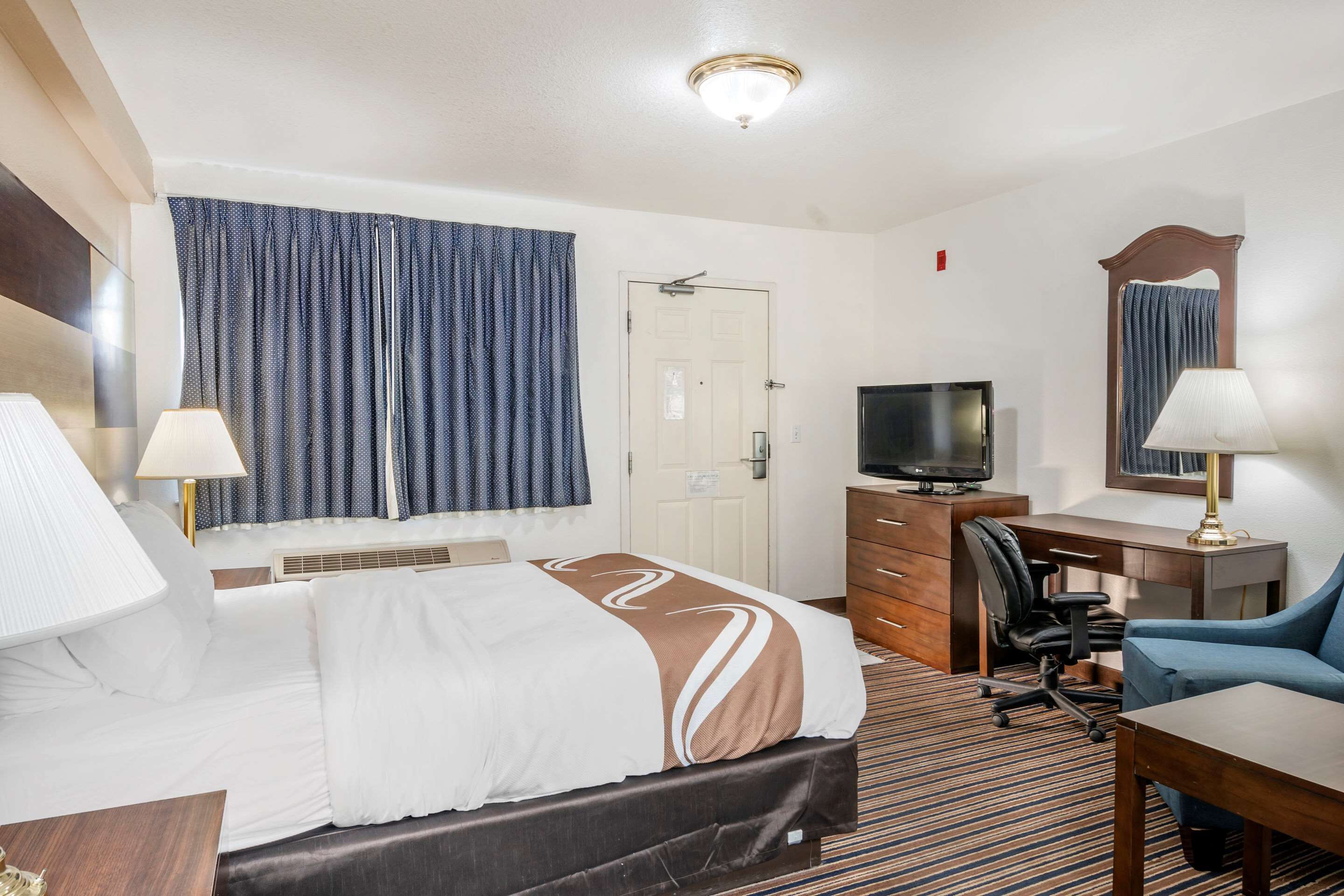 A hotel room with a bed, a desk, a chair, a television, and a mirror.