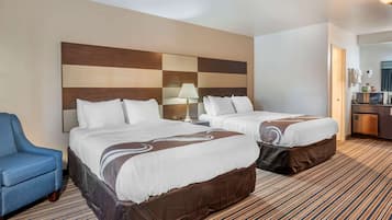 Une chambre d’hôtel avec deux lits, un fauteuil bleu, un bureau avec une lampe et un mini-bar.